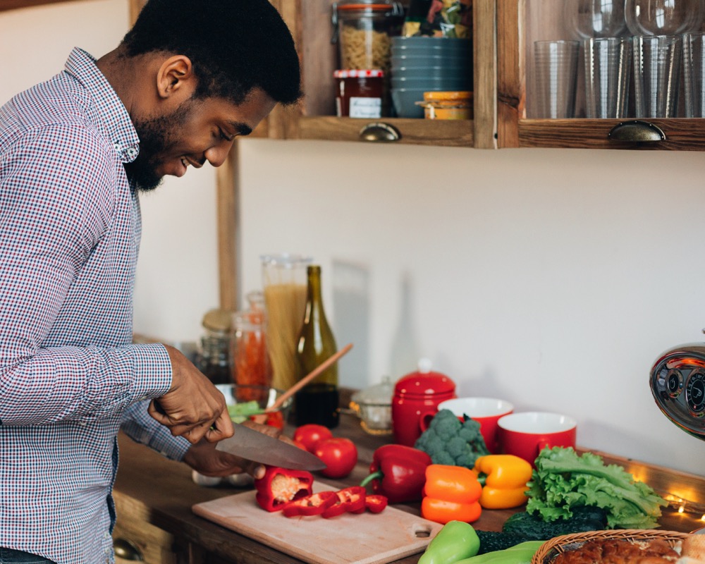 African-american man cutting bell pepper in kitchen stock photo